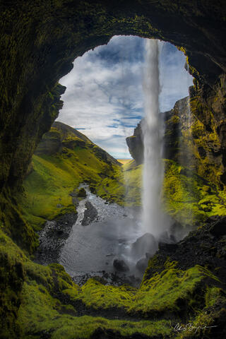 Waterfall viewed from behind as it cascades over the edge of the cliff and falls into the deep, narrow, lush green gorge.