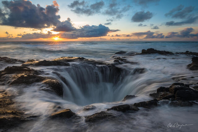 A tide pool drainage well along the Oregon coastline fills as waterfalls pour in against the black volcanic rock at sunset.