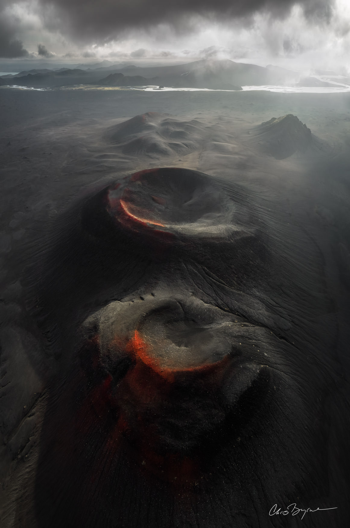 BREATHLESS CREATURES Aerial photograph of iceland highlands showing deep black dirt and crusted over cone of a dormant volcano with a red soil ring still seen around the edge.