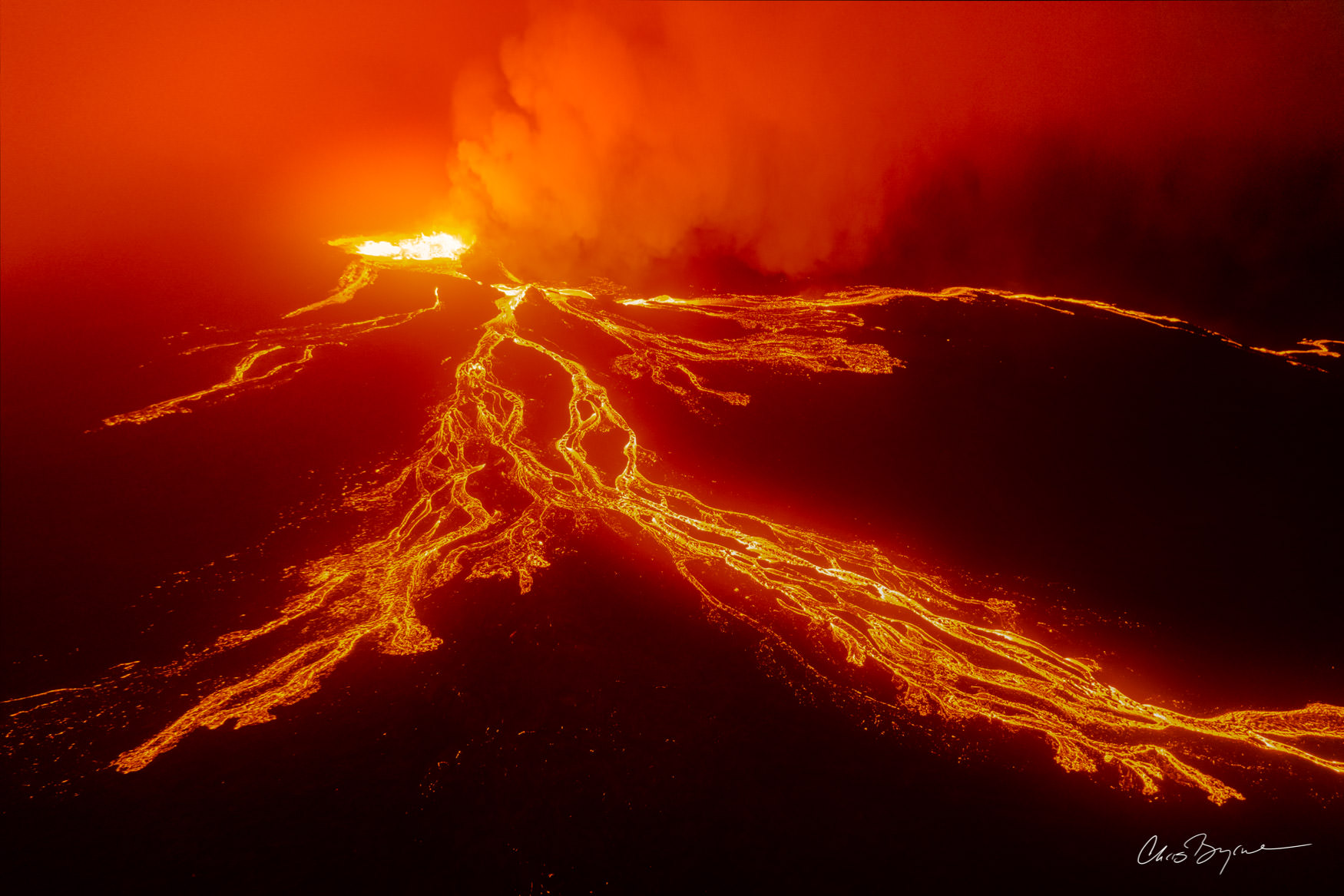 SEETHER Aerial photograph of a volcano at night shows finger-like orange lava flows and the bright orange molten lava bubbling out of the volcanic crater.