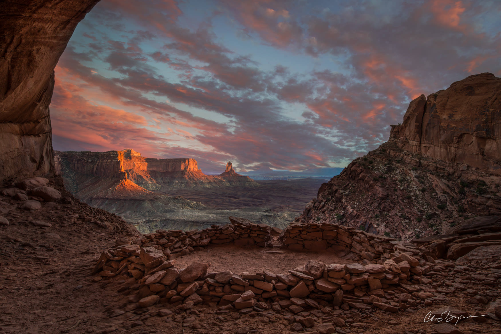 THE GODS ARE WATCHING A circle made of stone sits in a cave and from behind it are views of the desert landscape and sandstone rock formations found in Utah.