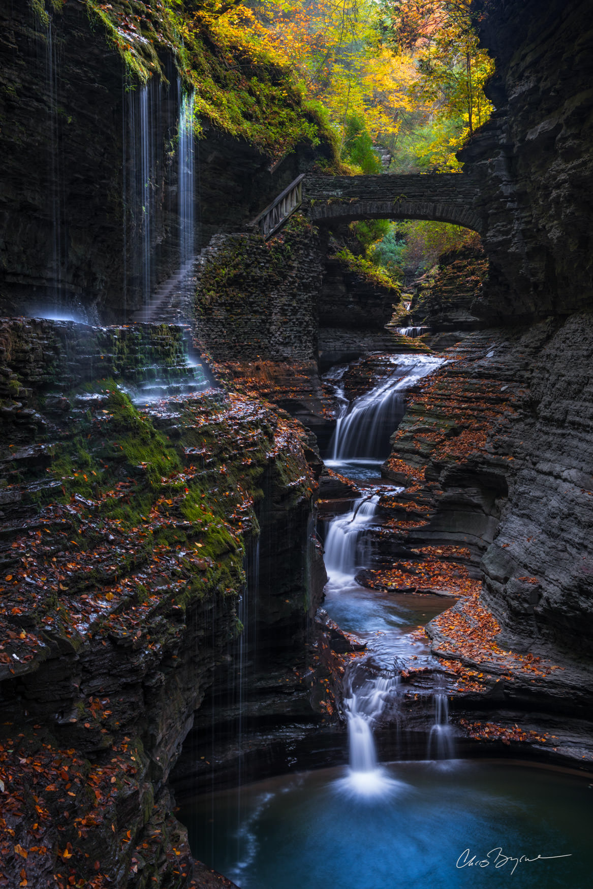 FALL UPON THE GLENN Multi-tiered waterfall with yellow leaves on the trees and red leaves on the steps of the wet, dark canyon walls as the water pools below.