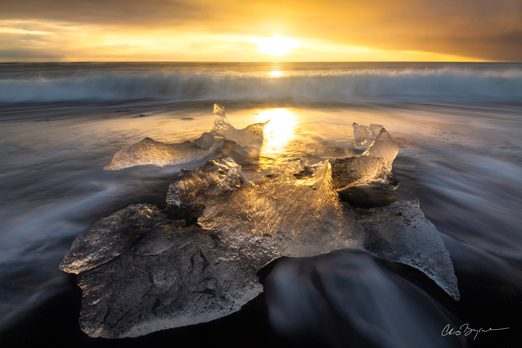 ICE CLAW Clear chunks of ice shine on a black sand beach in iceland as the sun rise lights them up and waves roll in on the cold south shore of Iceland.